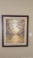 Full view of the framed birch tree painting showing the dark wood frame and beige mat with the landscape in warm yellow and brown tones.