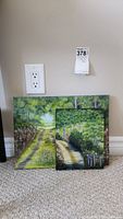 Two framed stretch canvas landscape paintings leaning against wall, showing paths and trees.