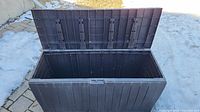 Open top view of black outdoor storage bin showing large interior space and plastic construction.