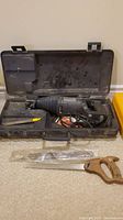 Photo showing reciprocating saw in carrying case with extra blades and hand saw laid out in front.