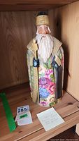 Full view of Santa figurine on a wooden shelf showing colorful floral patterns and traditional Russian attire.