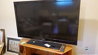 Samsung 46 inch LCD TV on wooden stand with remote control and power cable visible