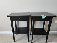 Two identical black wooden side tables placed against a wall showing front and side views.