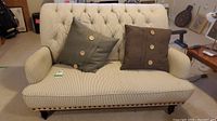Front view of small sofa with vertically striped fabric and two brown cushions with wooden buttons, rivet details along the bottom edge.