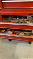 Three drawers of a red metal tool chest with assorted tools including drill bits, files, clamps, wrenches, tape measure, hammer, stapler and heat stripper.