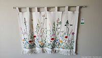 Full view of the full wall hanging embroidered with flowers and grasses, hanging from a metal rod.