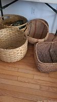 View of six woven baskets on wooden floor showing four large round baskets and two other baskets with handles