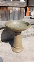 Concrete bird bath standing on a concrete surface outdoors, showing smooth finish and shape.