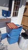 Photo showing blue storage totes stacked outside next to a multicolored serving tray and outdoor trash cans
