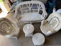 Full view of child's wicker furniture set including loveseat, two chairs, round table, and stool on floor.