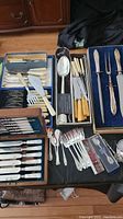 Overall view of multiple cutlery sets including mother of pearl handles, plastic handles, carving set, and serving utensils