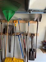 A variety of garden tools hung on a wall including shovels, rakes, cultivators, and a hoe.