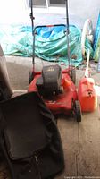 Front and side view of red Yard Machines lawn mower with attached fabric grass collection bag, red gas can, and orange funnel nearby.