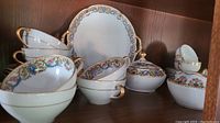 Overall display of white porcelain dinnerware with floral and gold trim including cups, saucers, plates, creamer, sugar bowl and platter