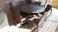 Full set: round metal dining table with six woven chairs and cushions on wood deck
