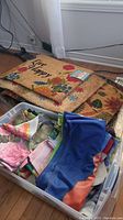 Stack of coir door mats with floral patterns and text 'Live Happy', visible rubber-backed mats underneath, with plastic bin containing colorful folded flags