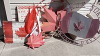 Arrangement of Canadian themed outdoor signs and flag on ground, showing wooden flag sign, metal maple leaves, Canadian fabric flag, and oval metal sign.