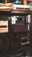 Multi-level shelving displaying rolled cloth screen at top, projector case in middle, stereo components and speakers on lower shelves.