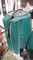 Front side view of green plastic rain barrel with hose attached