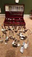 Full view of flatware pieces displayed in wooden canteen and spread out on carpet.