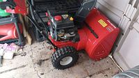 Side view of red steel housing, black engine and large treaded tires next to storage shed