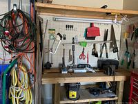 Photo of coiled extension cords in various colors, yellow rope, hand tools hanging on pegboard, and workbench with tools and light on it.