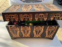 Wooden box with skeleton carvings on lid and sides, slightly open showing some toys inside.