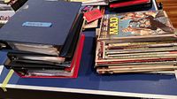 Five binders labeled as comics stacked on the left with a pile of loose magazines including MAD on the right
