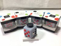 Four new in box light gray fidget cubes with red buttons visible in clear packaging and one cube outside the box shown from an angle