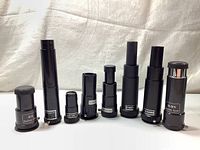 Front view of 7 black Barlow lenses arranged upright showing different heights and magnification markings.
