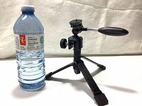 Photo of Bushnell tabletop tripod with pan tilt head next to a water bottle for size reference, showing tripod legs and mounting screw on top.