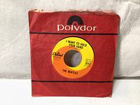 Front of the original red Polydor sleeve with the 7-inch vinyl record inside, showing the yellow and orange Capitol Records label 'I Want To Hold Your Hand'