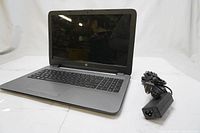 Front view of HP laptop open showing keyboard and screen, with power adapter beside it.