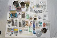 Overview of a large assortment of nails, nuts, bolts, fasteners and other hardware laid out on white surface. Shows quantity and variety of items included.