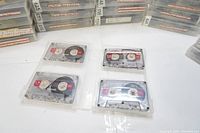 Close-up of four Maxell 90 minute UR model audio cassette tapes in clear plastic cases, showing tape reels and label detail.