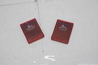 Two translucent red Magic Gate 8 MB memory cards for PlayStation 2 on white background.