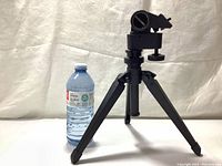 Side angle photo showing the tripod folded with one leg extended, and a water bottle placed beside for scale.
