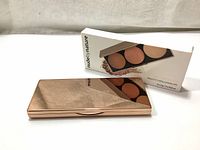 Photo of the closed rose gold metallic compact case of the Nude By Nature Highlight Palette along with its box.