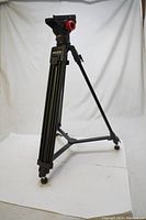 Full view of Optex Black tripod legs with fluid drag pan head, showing tripod structure and wheels at base.