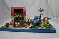 Front view of the assembled Playmobil farm set showing barn with red shingled roof, blue tractor, farm animals, figures, and various farm accessories including fenced areas and trees.