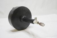 Side view of the black plastic drum with the coiled metal auger cable extending straight from the handle area