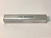 Silver box packaging of the Lise Watier concealer showing product name, size (2.5ml), and key features such as moisturizing and anti-fatigue.