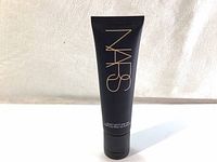 Front view of black tube of NARS Velvet Matte Skin Tint with gold logo on it against a plain background.