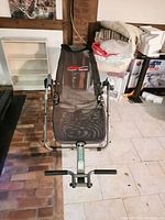 Front view of AB Lounge exercise equipment showing mesh seat and handlebars on a tiled and brick floor.