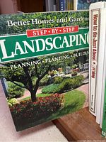 Close-up of book titled 'Better Homes and Gardens Step-by-Step Landscaping' alongside other books on a shelf.