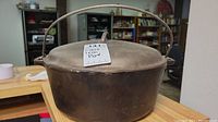 Photo of vintage cast iron pot with lid and bail handle sitting on a counter, showing overall condition and wear.