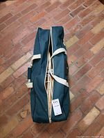 Closed dark green carrying bag for croquet equipment on brick floor.