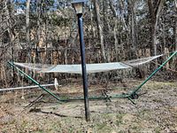 Full view of the hammock set up outdoors, showing metal frame and fabric sling with wheels on one end.