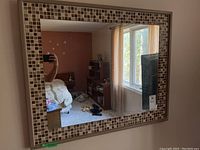 Front view of the rectangular mirror showing the mosaic tile border surrounding the clear mirror reflecting a bedroom interior.