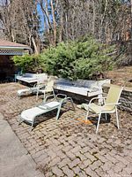 Photo shows two lounge chairs and two outdoor chairs on a paved outdoor area with a stone wall and greenery in the background